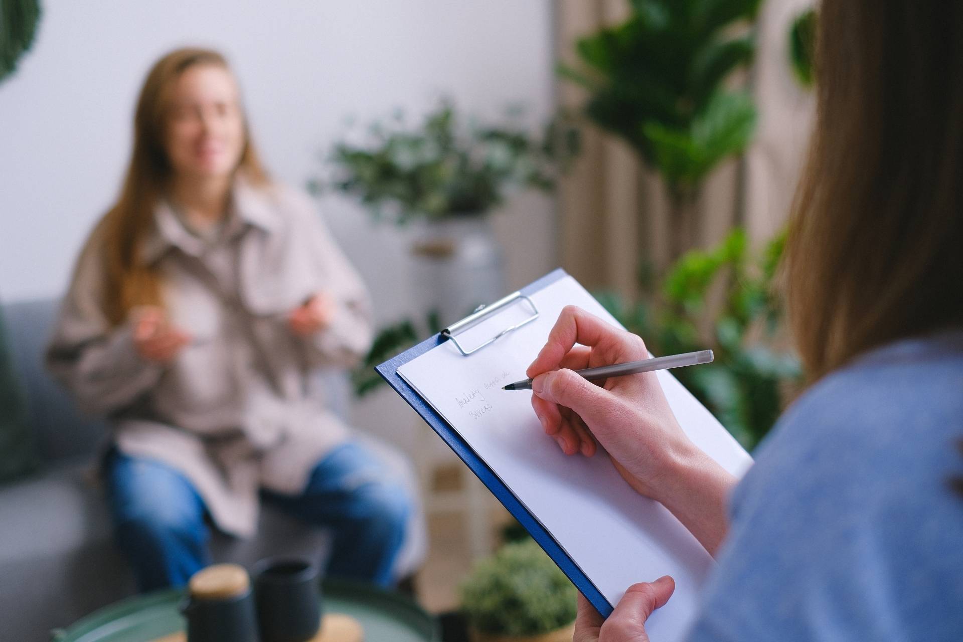 A woman on a couch expressing her trauma as a therapist takes notes during an inpatient healing therapy session.