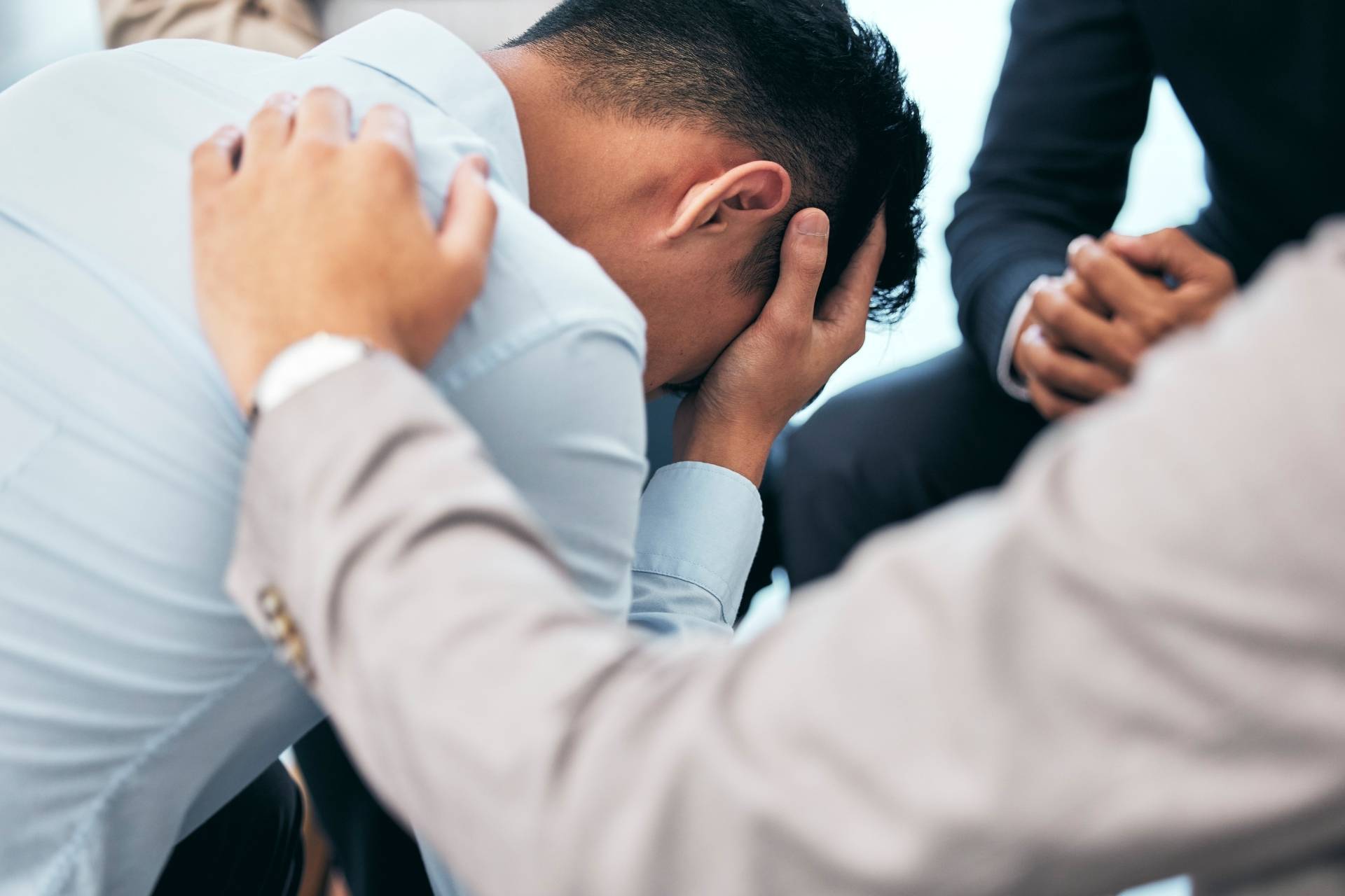 A depressed man sitting with his head in his hands as another man offers support, representing inpatient healing and emotional care.